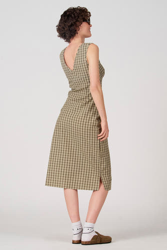 Groene mouwloze jurk van Unwind, met ruitpatroon en een split aan de zijkant, gedragen met witte sokken en bruine schoenen.
