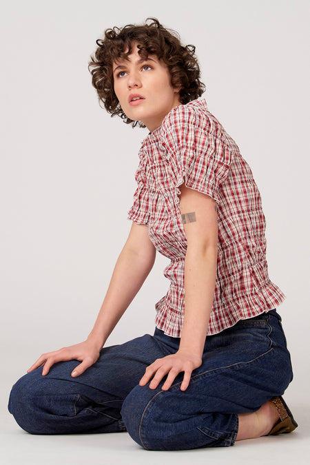 Rode blouse met korte mouwen van Unwind, met een ruitpatroon en ruches, gecombineerd met een donkerblauwe jeans.
