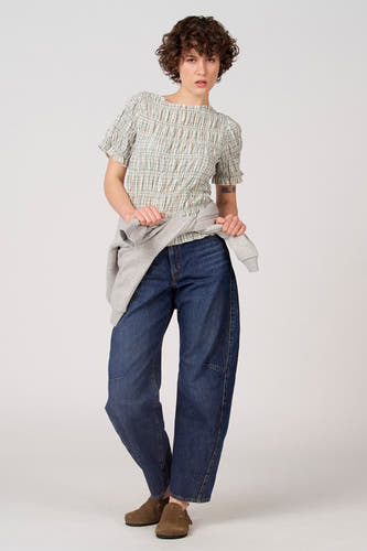 Chemisier vert à manches courtes d'Unwind, à motif à carreaux et détails smockés, porté avec un jean et un pull gris.