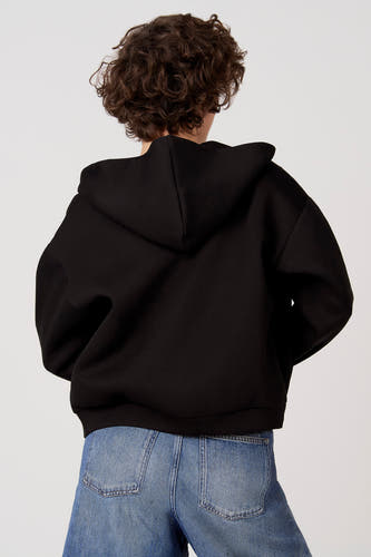 Zwarte sweater gilet van Unwind, gezien van achteren, met capuchon en gecombineerd met een blauwe jeans.
