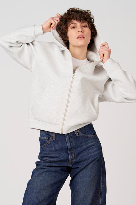 Grijs vest van Unwind, met een ritssluiting en capuchon, gedragen met een wit T-shirt en donkere jeans.
