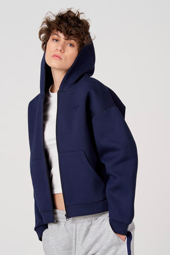 Blauw gilet van Unwind, met capuchon, zakken en een witte top en grijze joggingbroek eronder.