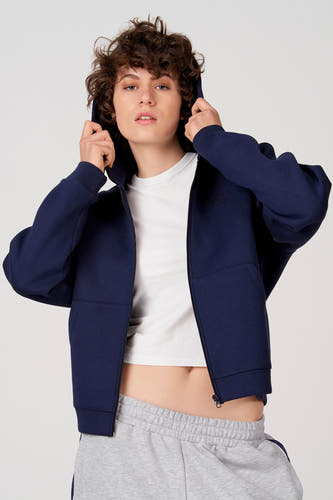 Blauw gilet van Unwind, met capuchon en ritssluiting, gedragen over een wit T-shirt en grijze joggingbroek.