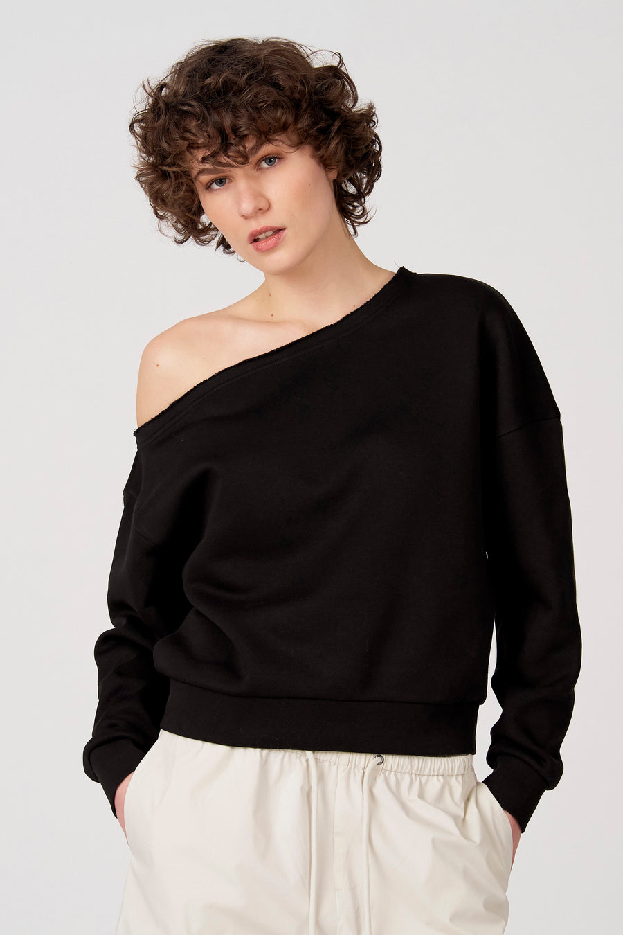 Zwarte sweater van Unwind, met een losse schouder en gedragen met een witte broek.
