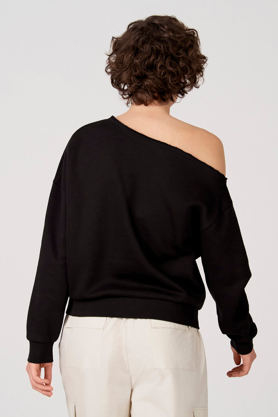 Zwarte sweater van Unwind, met een losse schouder en gedragen met een lichte broek.