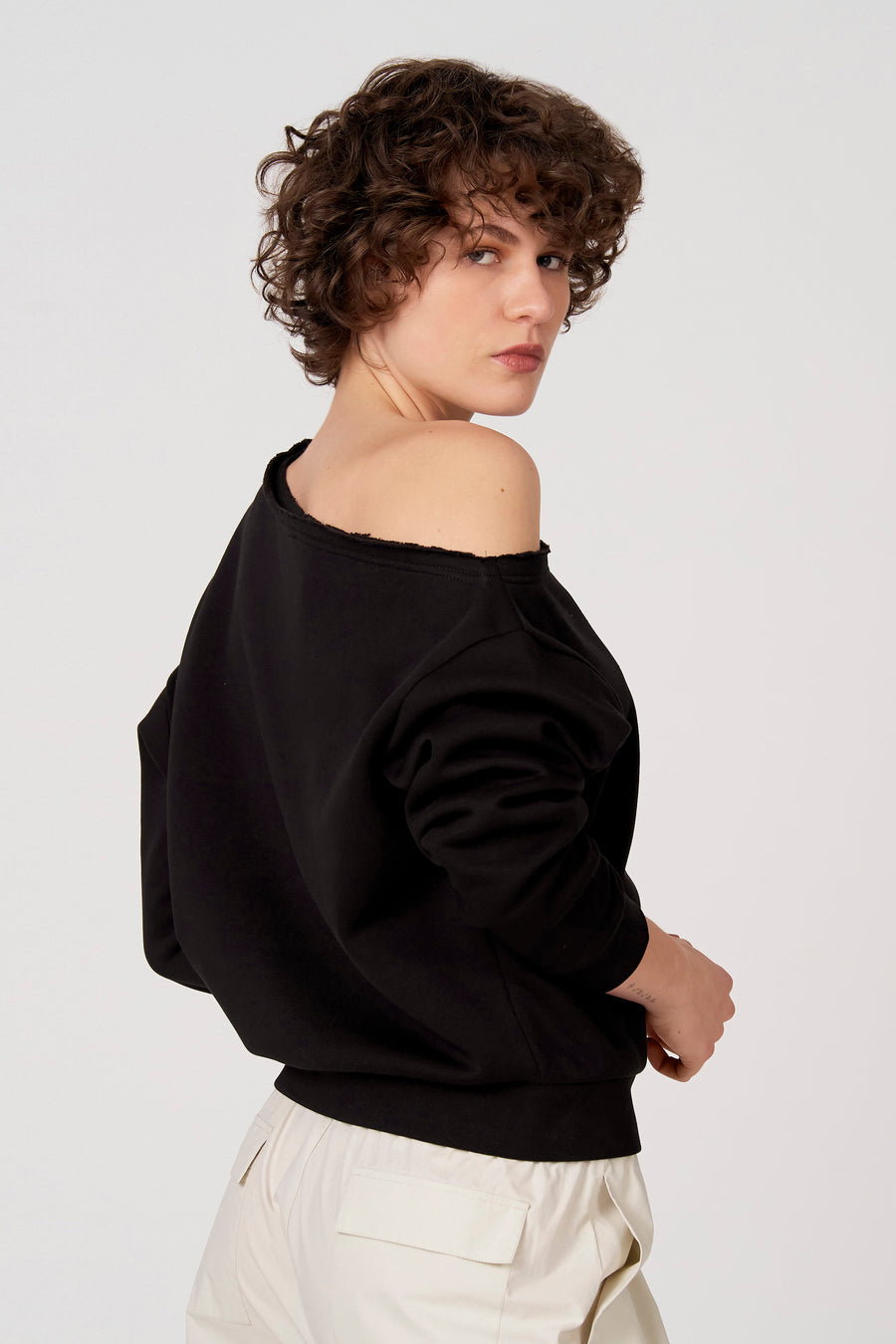 Zwarte sweater van Unwind, met een losse halslijn en gedragen met een witte broek.
