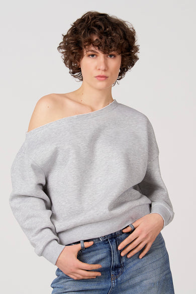 Pull gris Unwind, avec une épaule dénudée et associé à un jean.