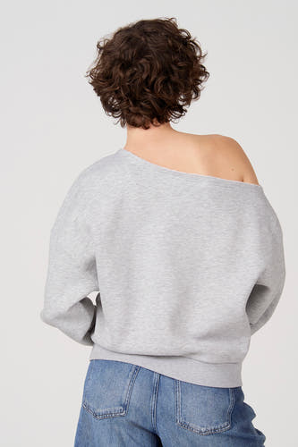 Grijze sweater van Unwind, met een blote schouder en gecombineerd met een jeans.