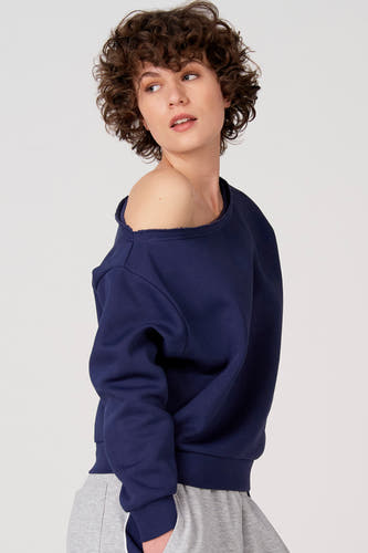 Blauwe sweater van Unwind met open schouder, gecombineerd met een grijze joggingbroek, zij aanzicht.
