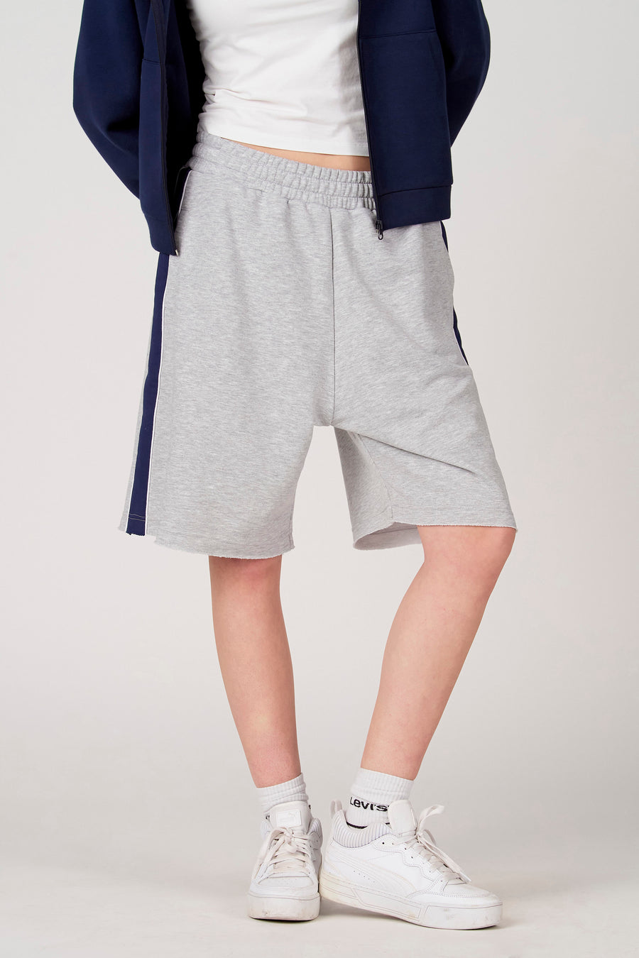 Short gris Unwind, avec une bande bleu foncé sur le côté et un bord effiloché, combiné avec des baskets et des chaussettes blanches.