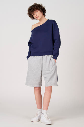 Short gris d'Unwind, avec un passepoil bleu foncé sur le côté et porté avec un pull bleu foncé et des baskets blanches.