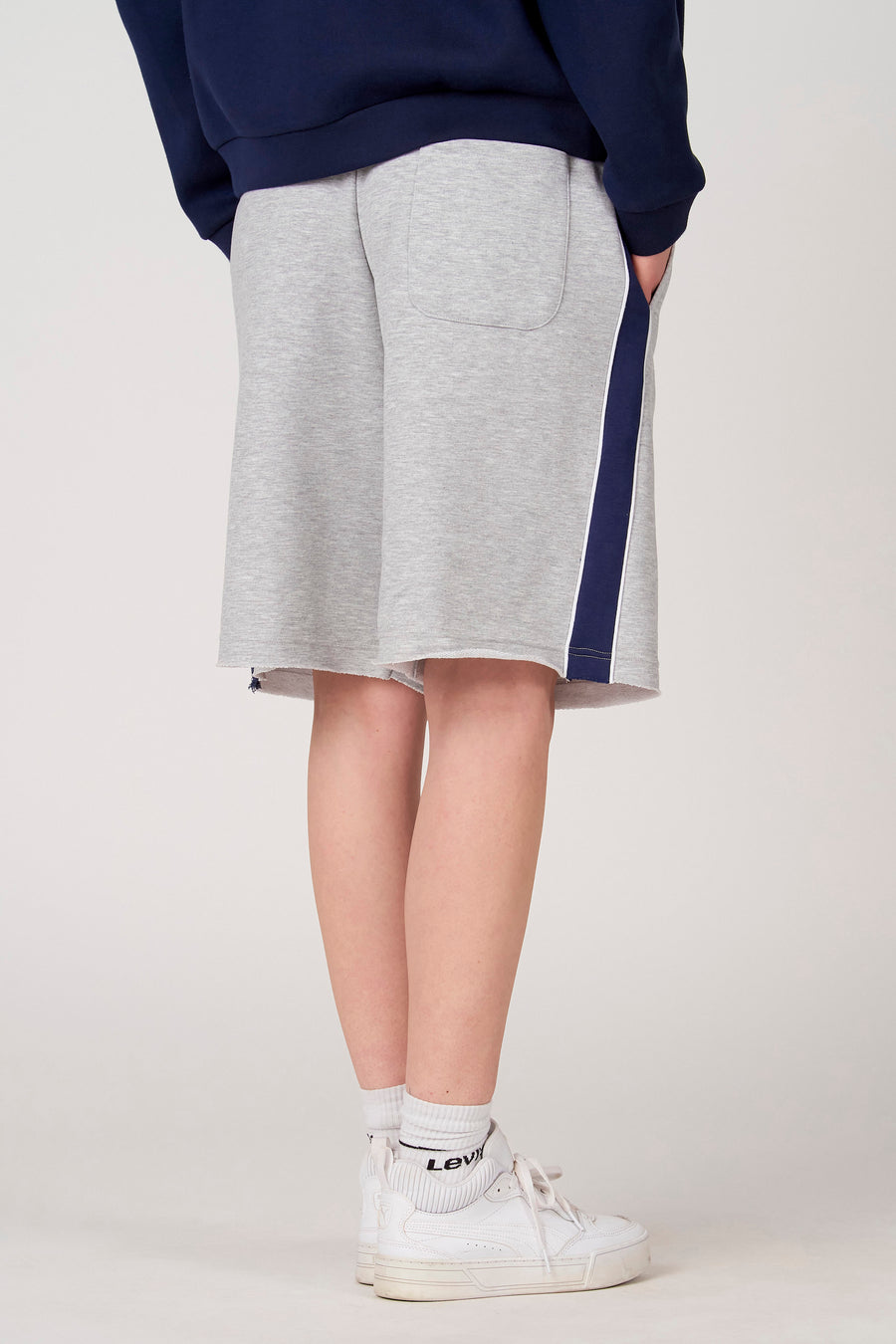 Short gris Unwind, avec une bande bleu foncé et blanche sur le côté, combiné avec des baskets et des chaussettes blanches.