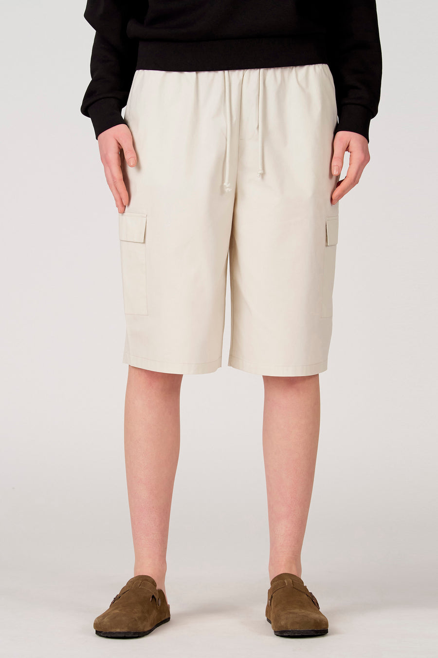 Short écru Unwind avec cordon de serrage à la taille et poches latérales plaquées, porté avec un sweat-shirt noir et des sabots marron.