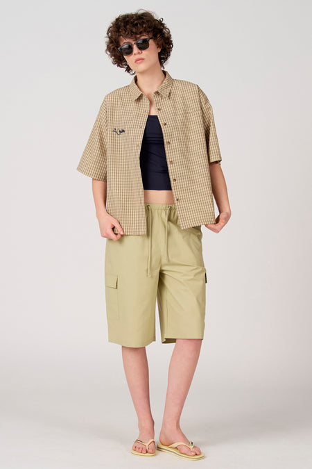Short cargo vert de Unwind avec cordon de serrage, stylé avec une chemise à carreaux ouverte.