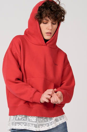 Sweat-shirt à capuche rouge d'Unwind, avec une poche kangourou à l'avant et porté sur un chemisier en dentelle blanche.