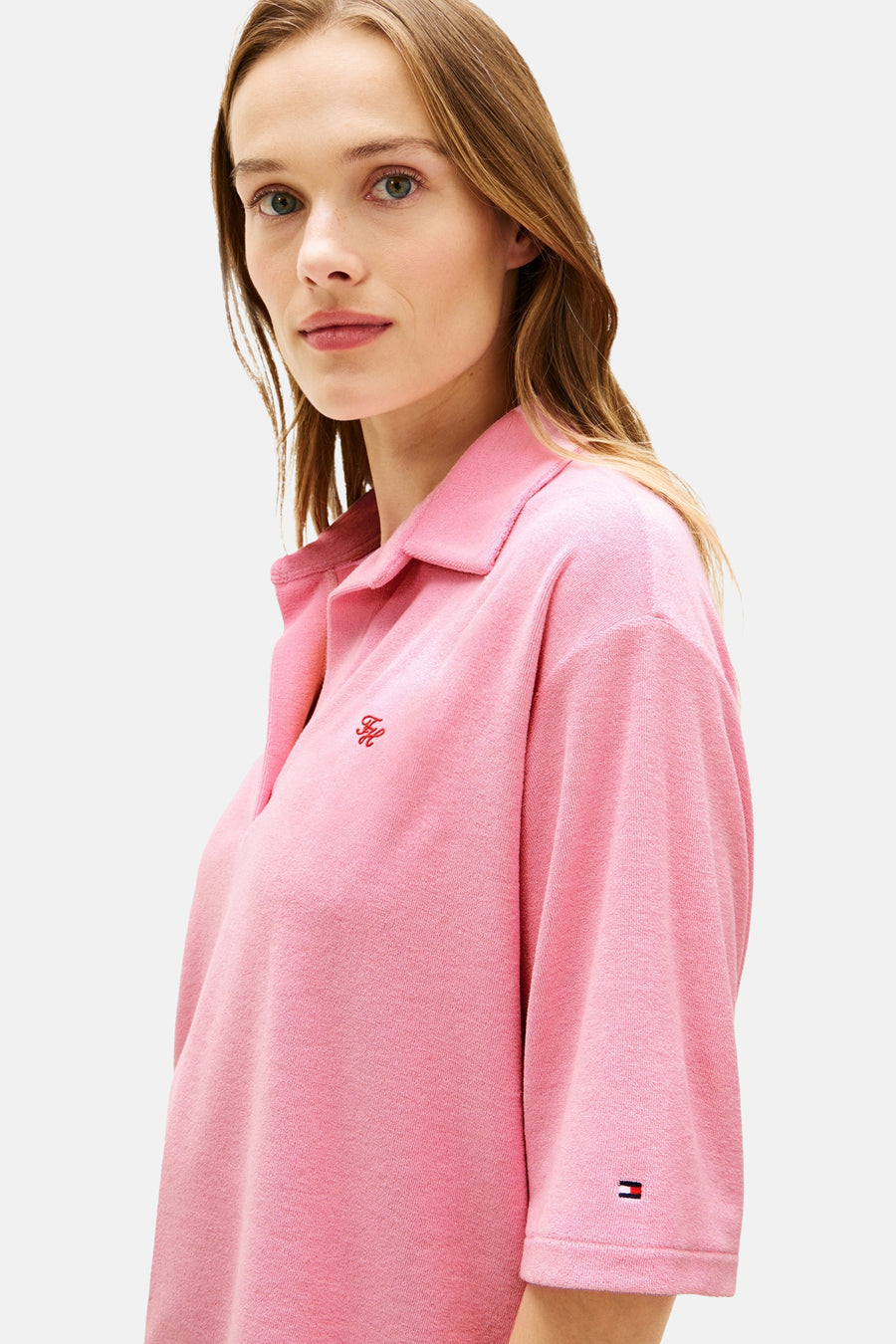 Roze polo met korte mouwen van TOMMY JEANS, gemaakt van badstof met een rood geborduurd FH-logo en een vlaglogo op de mouw.
