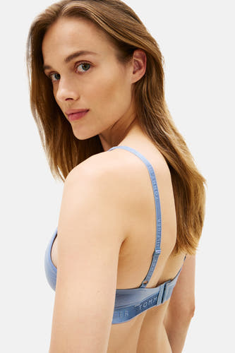 Blauwe beha van TOMMY JEANS, met merklogo op de bandjes, gedragen door een model dat over de schouder kijkt.
