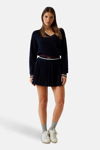 Blauwe korte rok van Guess, met plooien en een tailleband met het Guess-logo, gecombineerd met een trui en sneakers.
