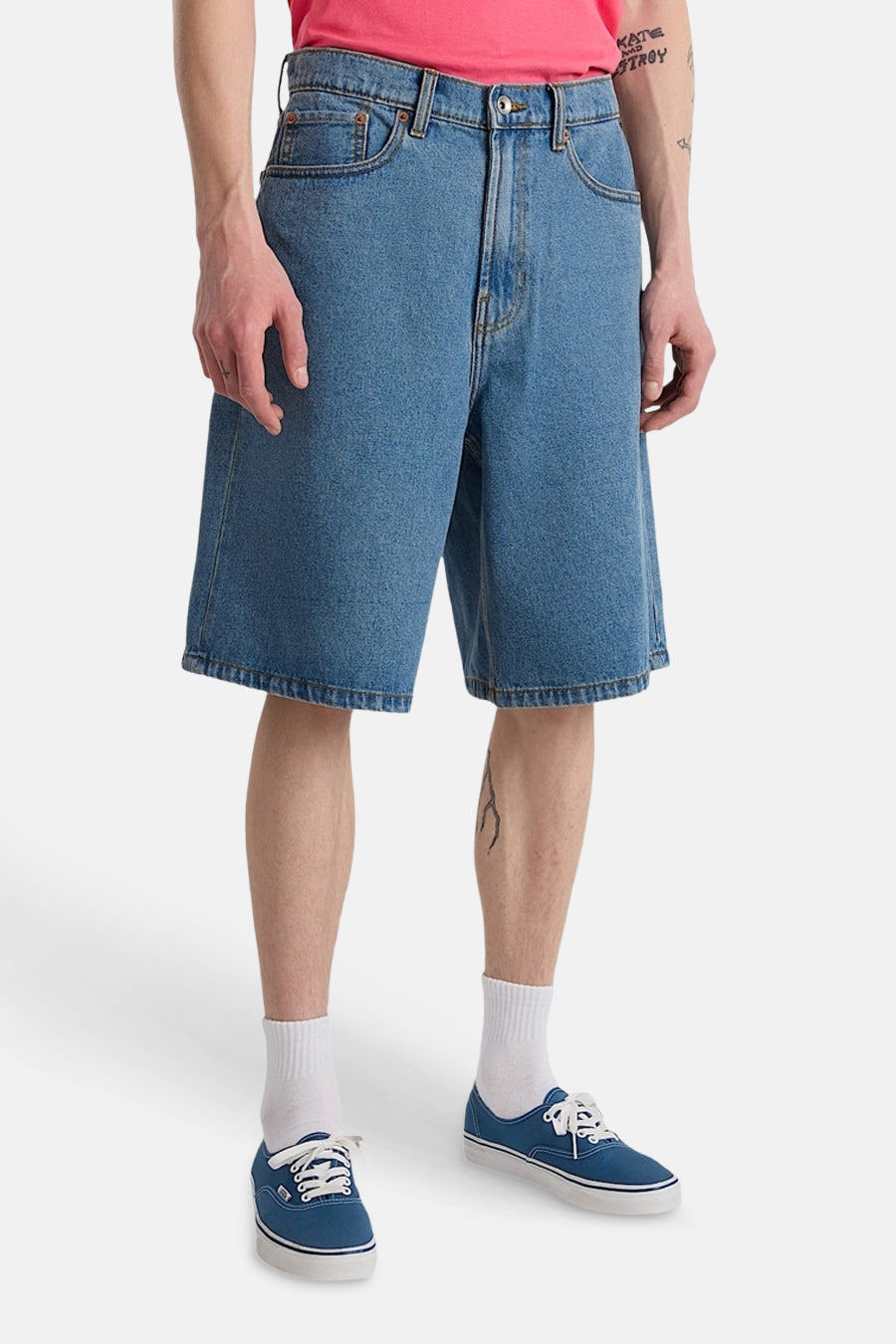 Short en jean bleu clair de VANS "OFF THE WALL" avec poches arrière plaquées, porté par une personne tatouée avec des chaussures en toile bleue.