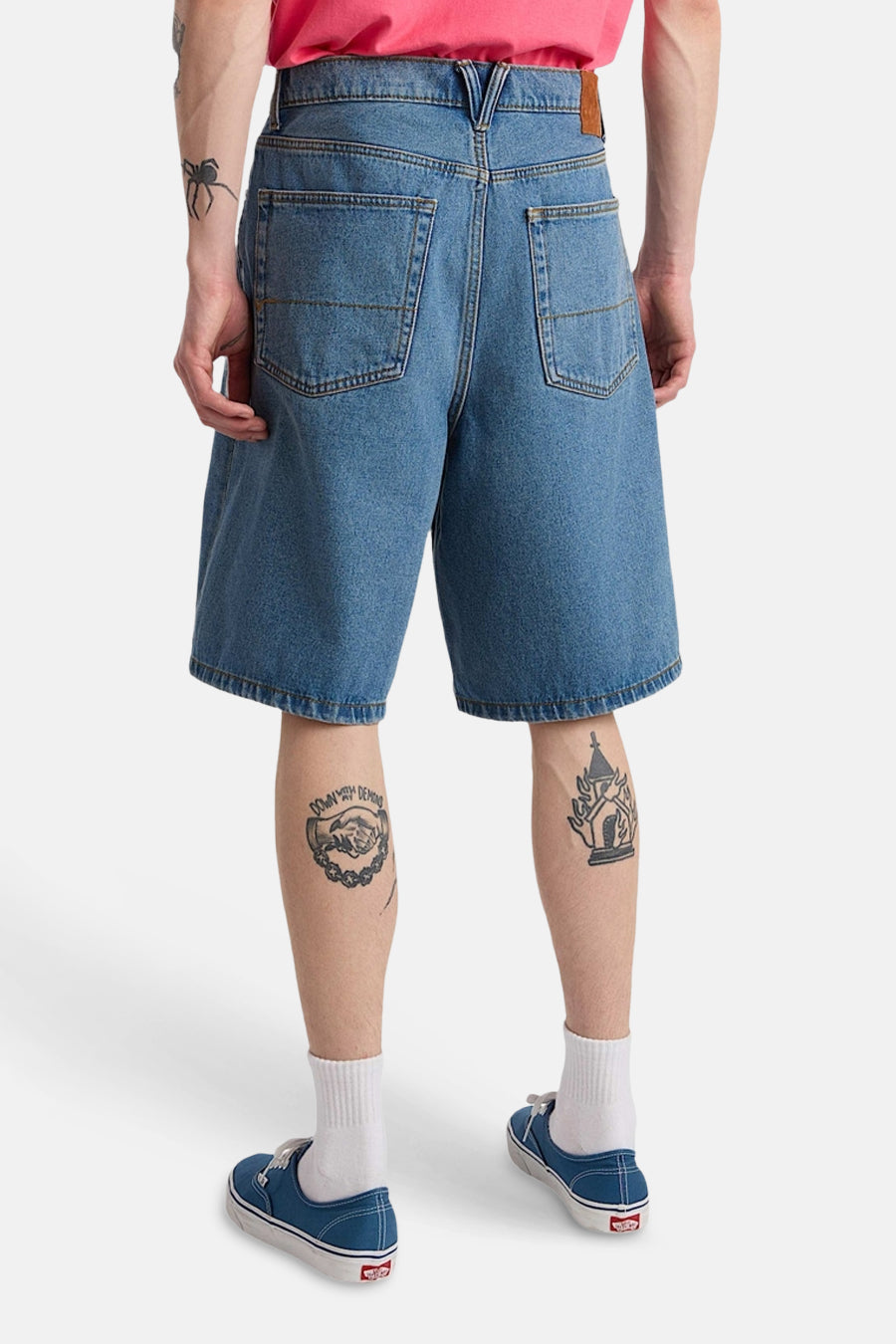 Lichtblauwe denim short van VANS “OFF THE WALL” met opgestikte achterzakken, gedragen door een persoon met tatoeages en blauwe canvas schoenen.