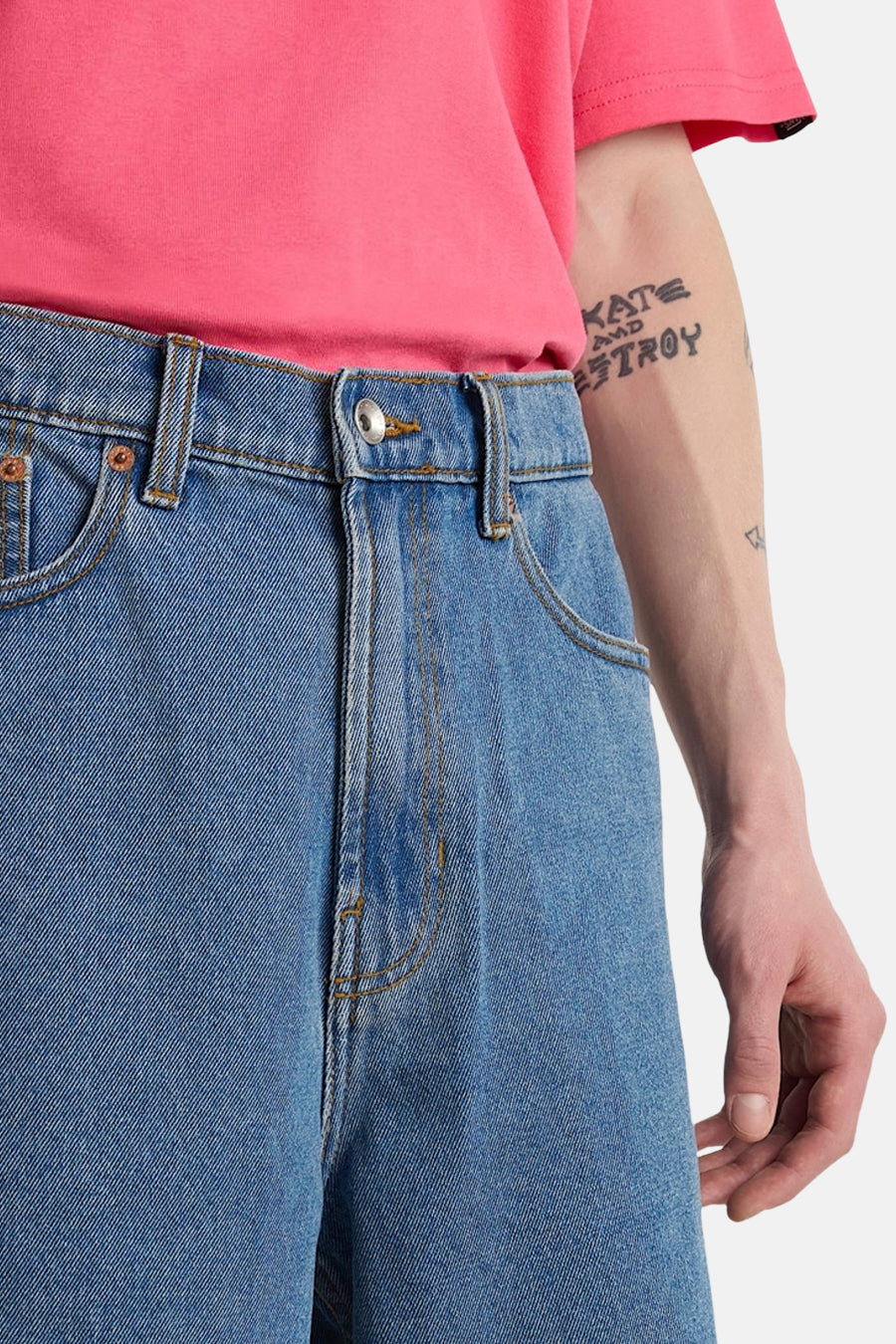 Short en jean bleu clair VANS "OFF THE WALL" avec bouton argenté, un t-shirt rose et un bras tatoué.