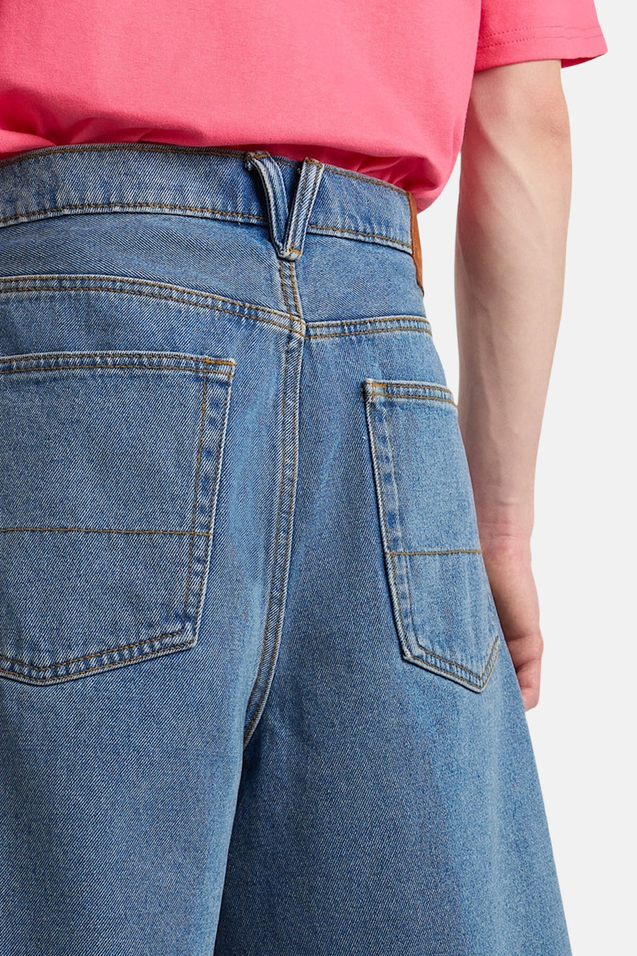 Short en jean bleu clair de VANS "OFF THE WALL" avec ceinture en forme de V, poches arrière plaquées et t-shirt rose, vue arrière.