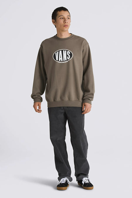 Bruine sweater van VANS “OFF THE WALL”, met een ovaal logo op de borst, gecombineerd met een grijze corduroy broek en zwarte sneakers.
