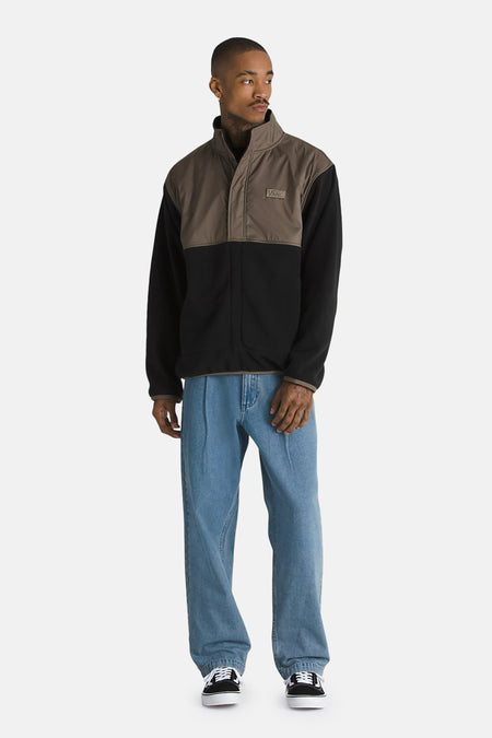 Veste en polaire à blocs de couleurs marron et noir de Vans avec col montant et écusson logo, portée avec un jean ample et des baskets.