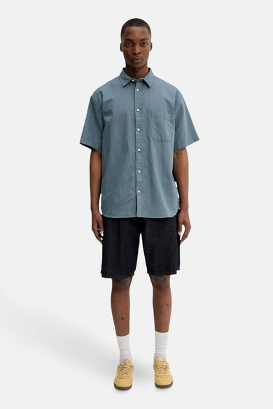 Chemise grise à manches courtes de VANS "OFF THE WALL", portée avec des shorts en denim, des chaussettes blanches et des baskets jaunes.