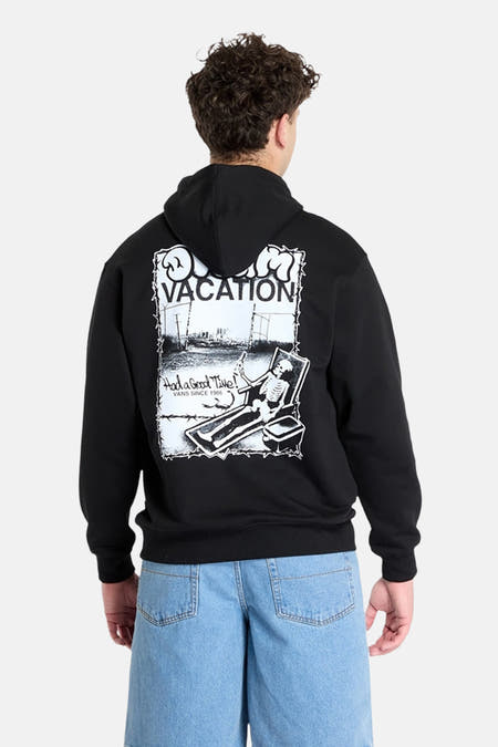 Zwarte sweater met kap van Vans, met een grafische print op de achterkant en blauwe jeans.
