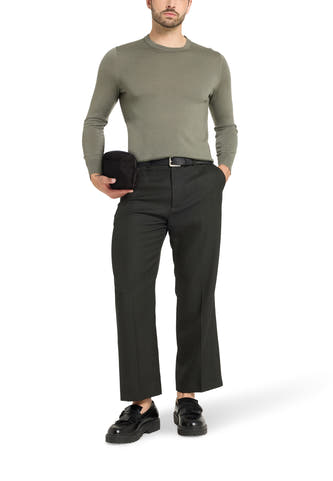 Zwarte schoudertas van VANS “OFF THE WALL”, gehouden door een model in een olijfgroene trui en donkergrijze pantalon.