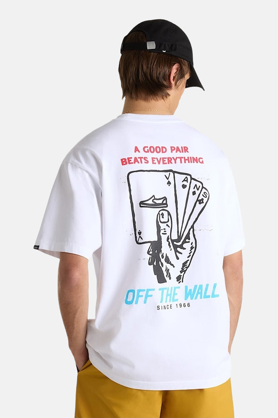 Wit T-shirt met korte mouwen van VANS “OFF THE WALL”, met grafische print op de rug en een zwarte baseballpet.
