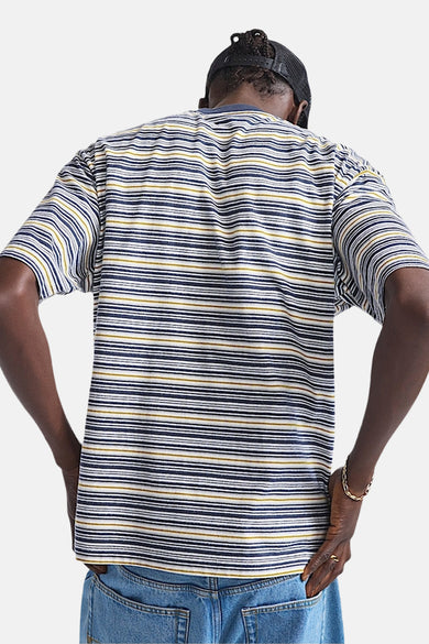 T-shirt bleu à manches courtes de VANS "OFF THE WALL", avec des rayures horizontales, porté avec un jean et une casquette noire.