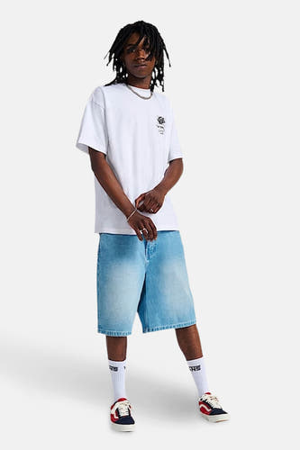 T-shirt blanc de VANS "OFF THE WALL", porté avec des shorts en denim bleu, des chaussettes blanches et des baskets colorées.