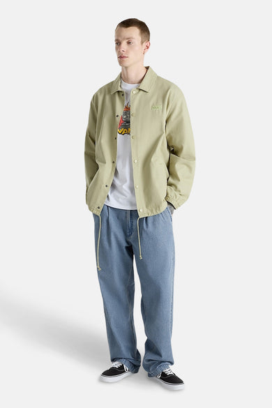 Jean baggy en denim bleu de VANS "OFF THE WALL", porté avec un manteau crème et un T-shirt blanc.