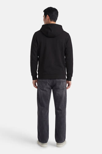 Zwarte sweater met kap van VANS “OFF THE WALL”, gezien vanaf de achterkant, met donkere jeans en lichte sneakers.
