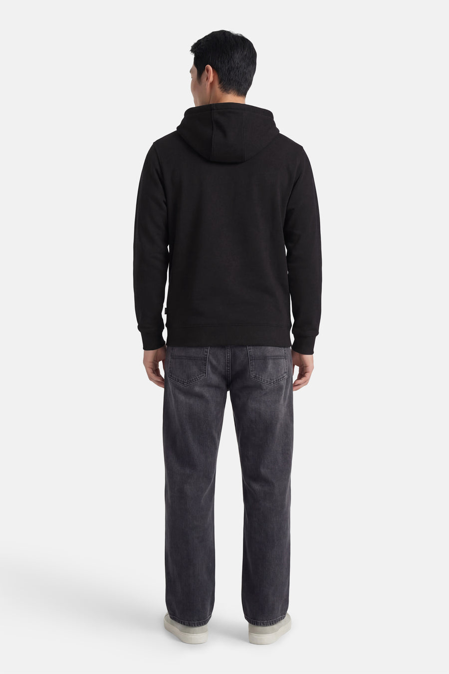 Zwarte sweater met kap van VANS “OFF THE WALL”, gezien vanaf de achterkant, met donkere jeans en lichte sneakers.
