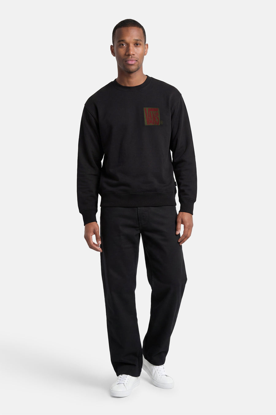 Zwarte sweater met ronde hals van VANS “OFF THE WALL” met rood-groen VANS-logo op de borst, gedragen met zwarte broek en witte sneakers.