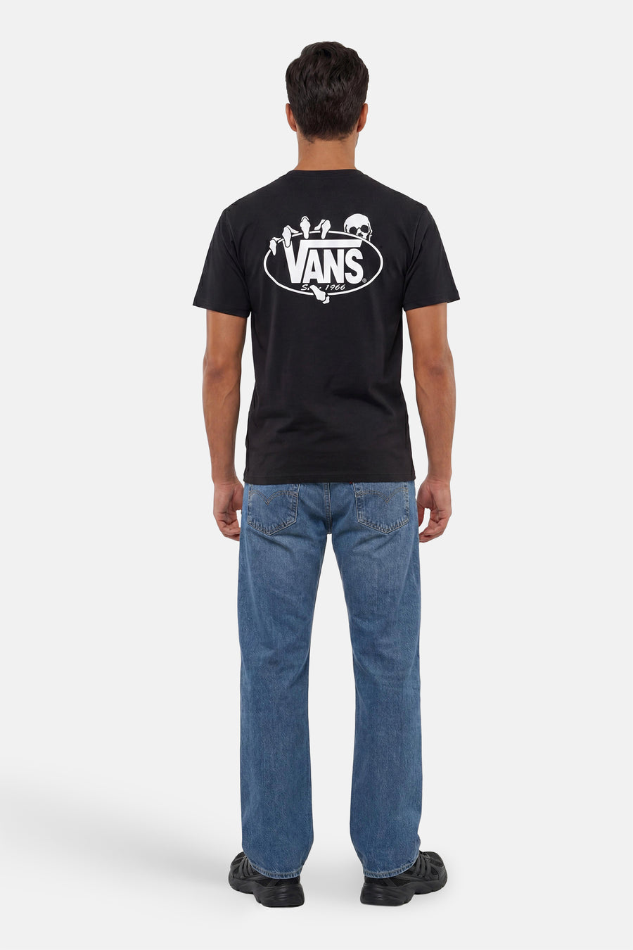 Zwart T-shirt van VANS “OFF THE WALL” met groot wit logo en skeletprint op de rug, gedragen door een man met blauwe jeans.