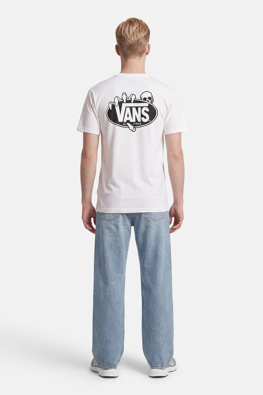 Wit T-shirt van VANS met schedel- en handopdruk op de rug, gedragen met een lichtblauwe jeans en grijze sneakers.