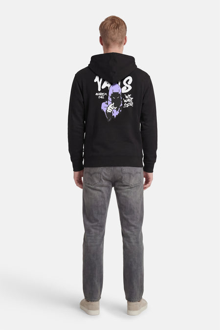 Zwarte sweater met kap van VANS “OFF THE WALL”, met print op de achterkant, gecombineerd met grijze jeans en beige schoenen.
