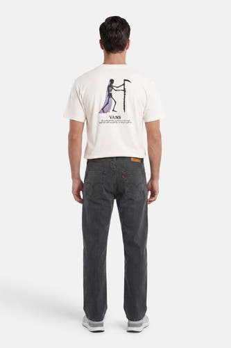 Ecru T-shirt van VANS “OFF THE WALL” met skeletprint en tekst op de rug, gedragen door een man in geribbelde jeans en sneakers.