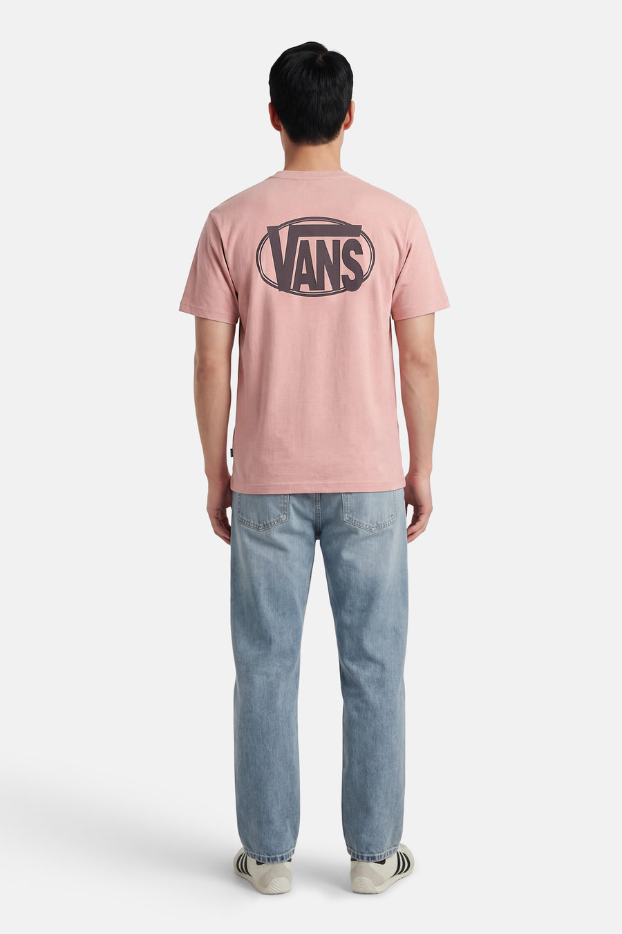 Roze T-shirt van VANS “OFF THE WALL” met een groot logo op de achterkant, gedragen met blauwe jeans en witte sneakers.