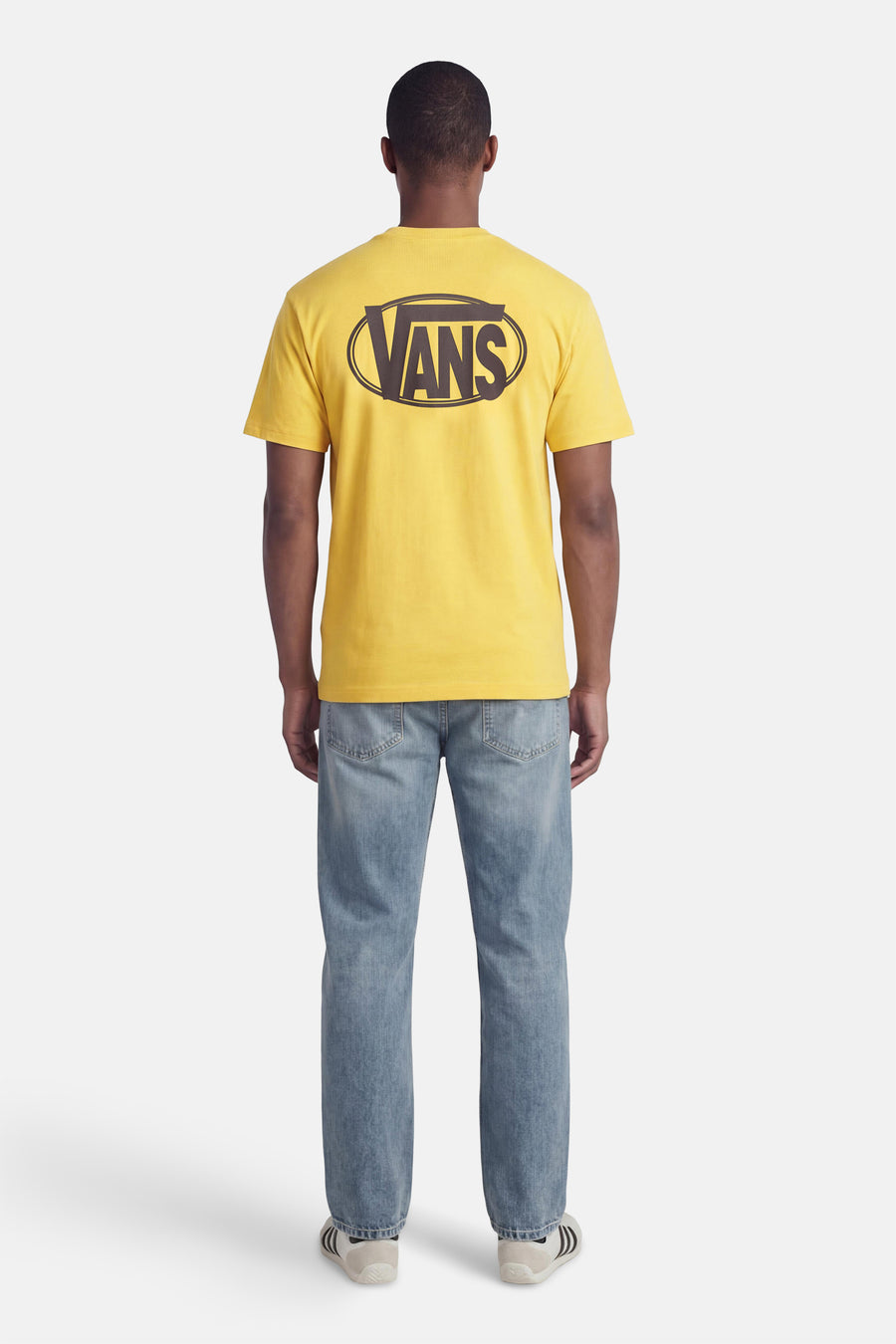 Geel T-shirt met korte mouwen van VANS "OFF THE WALL", met een ovale graphic op de rug, gedragen met jeans en sportschoenen.
