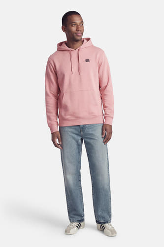 Roze sweater met kap van VANS “OFF THE WALL”, met lange mouwen, buidelzak en blauwe jeans.