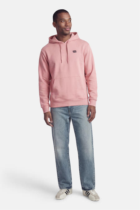Roze sweater met kap van VANS “OFF THE WALL”, met lange mouwen, buidelzak en blauwe jeans.