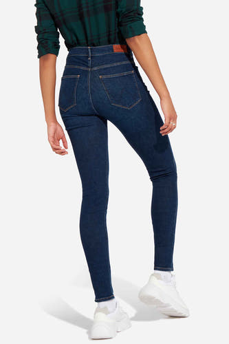 Jean skinny bleu foncé - denim de Wrangler, vu de dos, avec une chemise à carreaux verte et des baskets blanches.