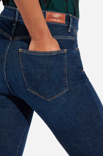 Jean skinny en denim de Wrangler, avec une poche arrière où une main peut tenir, et un logo en cuir marron.