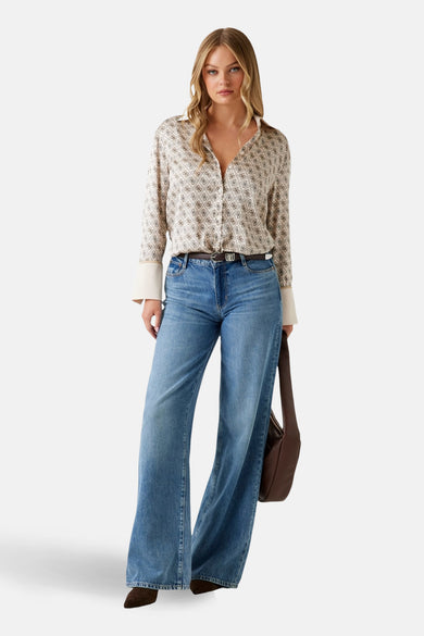 Beige hemd met lange mouwen van Guess, met een print en witte manchetten, gedragen met een bruine riem en blauwe jeans.
