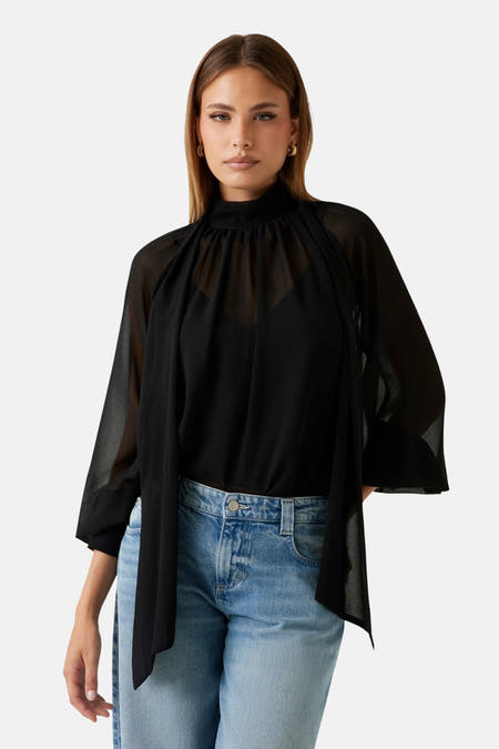 Zwarte blouse met lange mouwen van Guess, met een doorschijnende stof en gedragen met een blauwe jeans.
